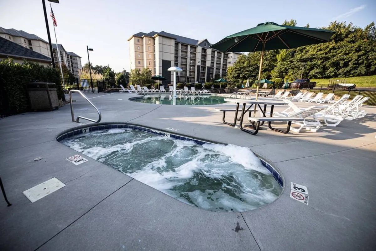 The image captures a vibrant pool area featuring a hot tub, swimming pool, lounge chairs, a picnic table, and an umbrella, set against a backdrop of the resort's grounds. The scene conveys a sense of fun, relaxation, and social gathering.