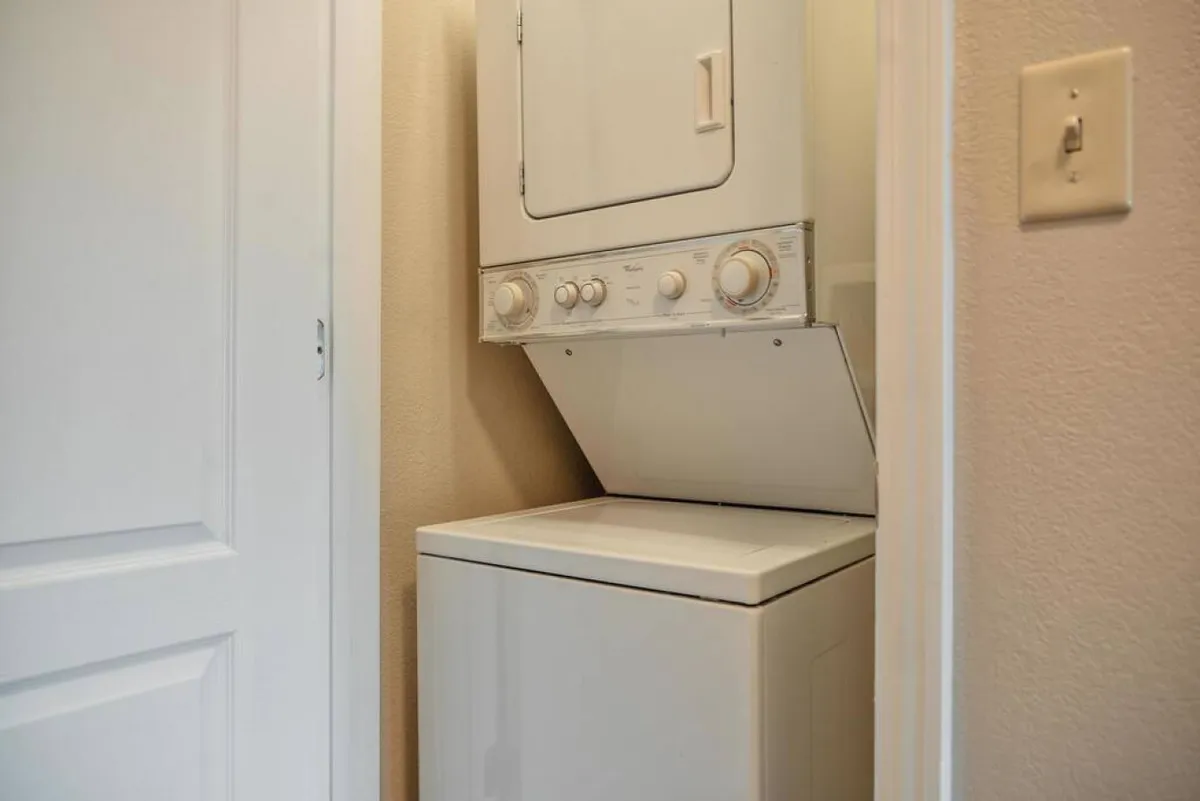 A compact and efficient laundry area with a stacked washer and dryer against crisp white walls. The space is clean, organized, and accessible, emphasizing convenience for guests.
