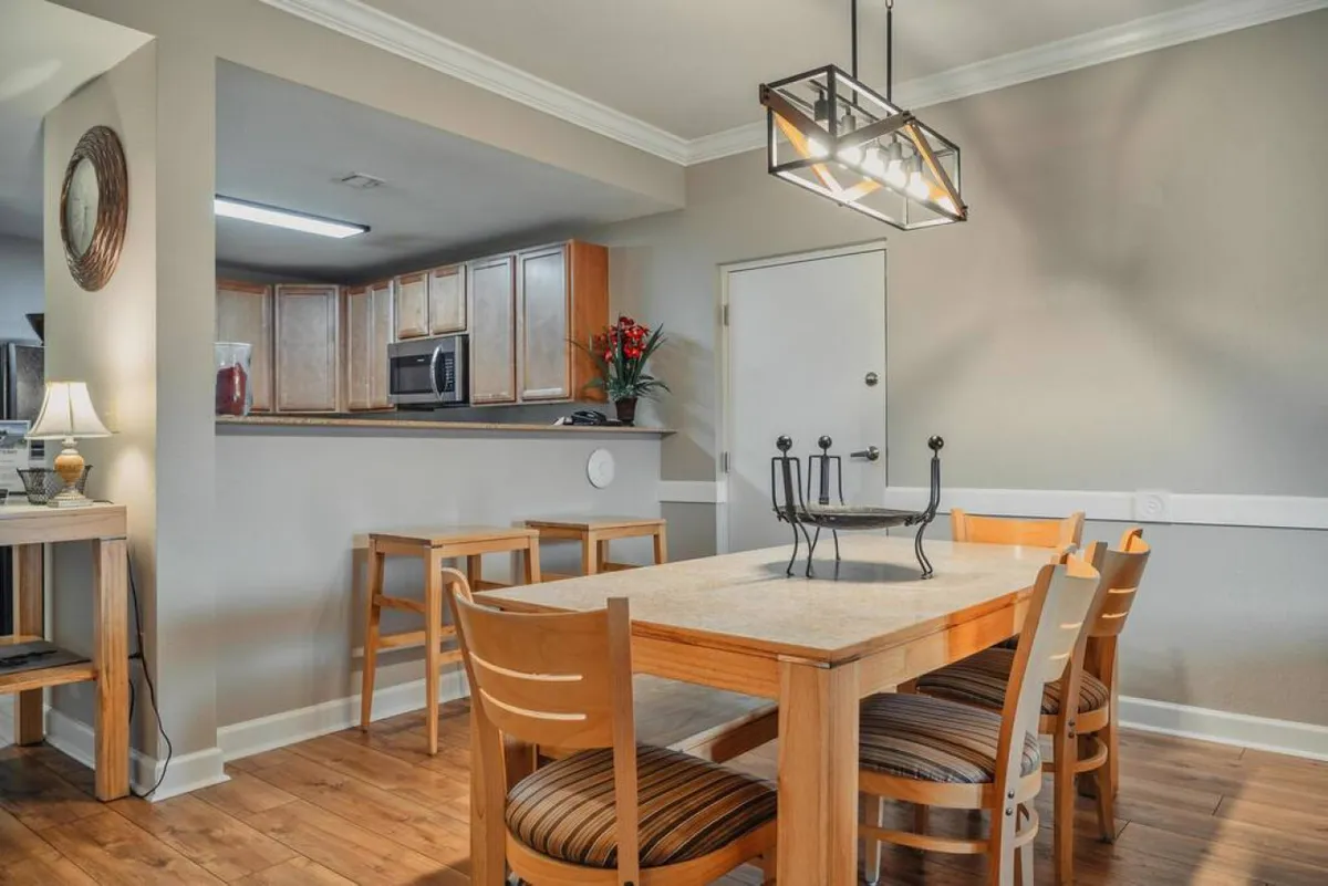 A cozy dining area with a prominent dining table, stylish lighting above, and a view of the kitchen bar in the background. The layout encourages communal dining and conversation, ideal for family meals or festive gatherings.
