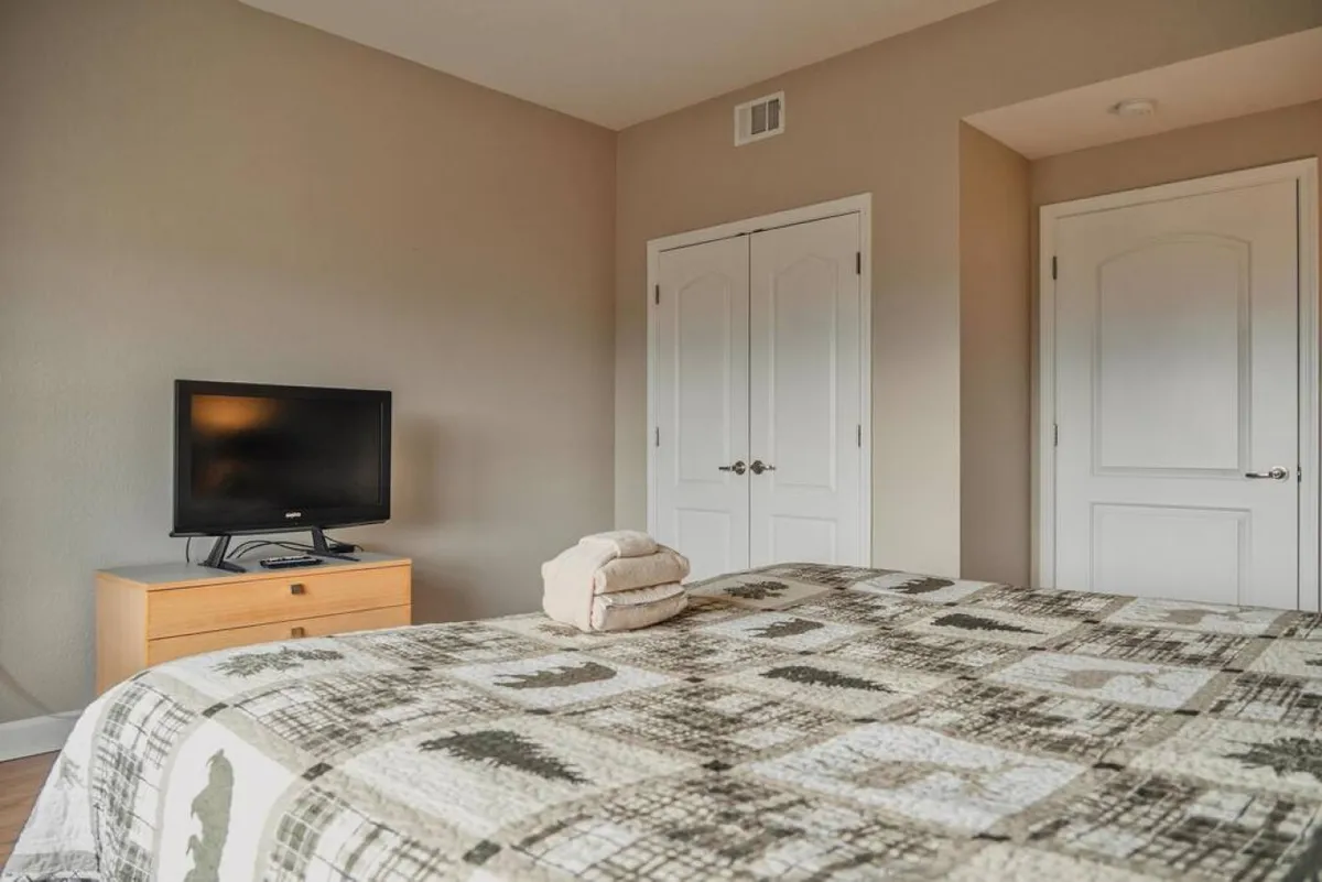 A comfortable bedroom featuring a bed with a patterned quilt, a television on a stand, and closet doors, exuding a welcoming and functional vibe well-suited for guests or family members.
