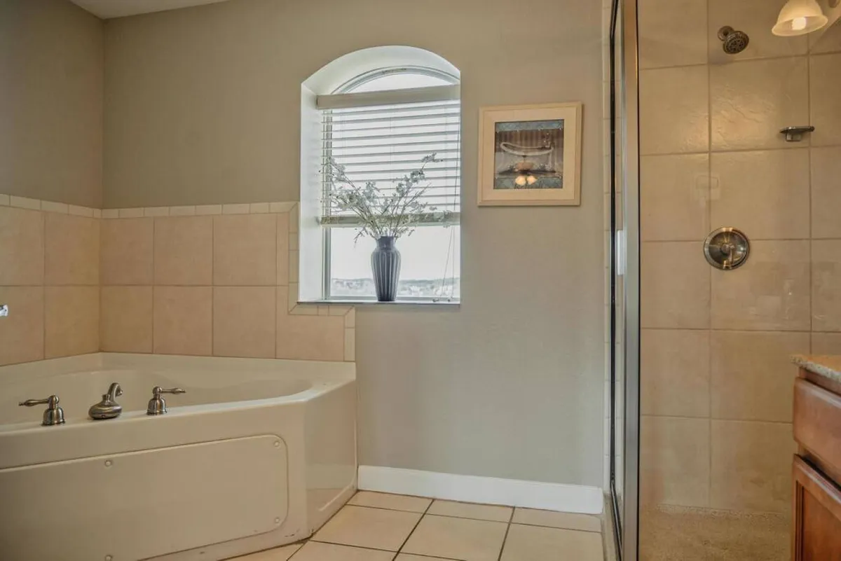 A tranquil bathroom scene with a bathtub and separate shower area, a window with a view, a decorative plant, and framed wall art, offering a spa-like retreat perfect for unwinding after a long day.