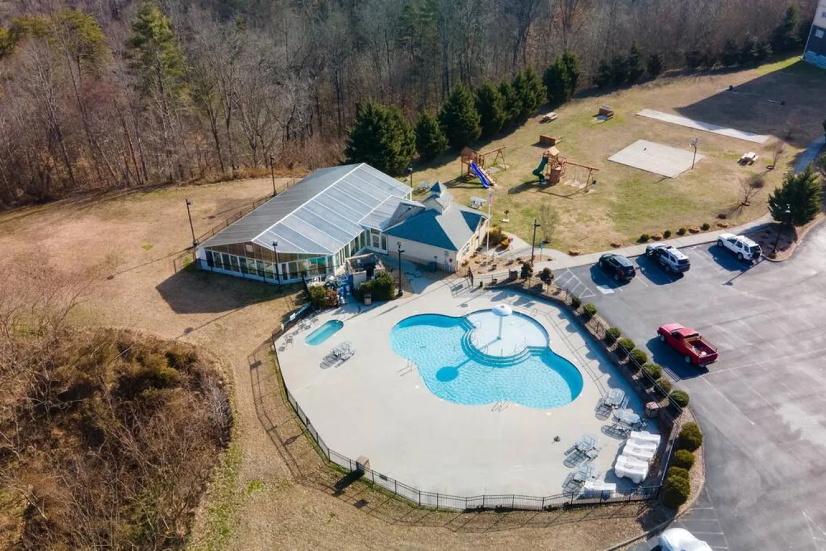 An outdoor pool area with sunbathing spots, an adjacent play area, and a recreation center in the background. Children can be seen playing, with families gathering nearby, evoking a sense of joyful, communal fun.